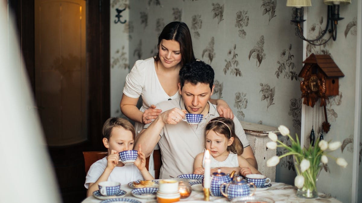 Contented family drinking tea with crepes together while sitting at table with candles at cozy kitchen with cuckoo clock on wall